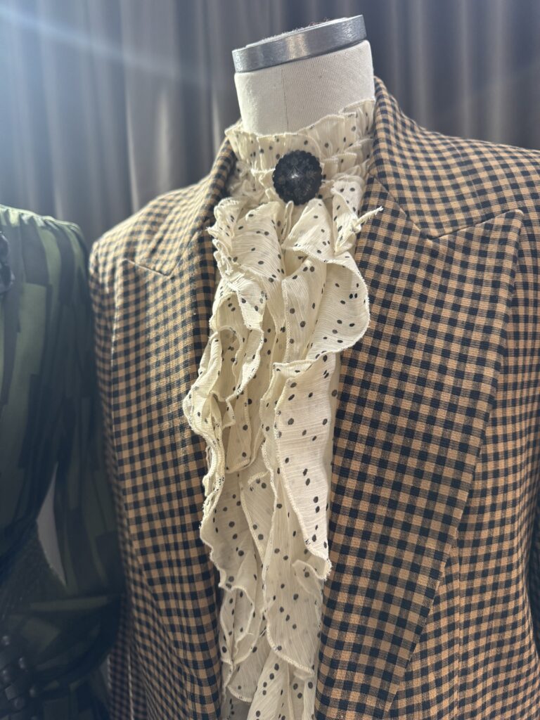 En skyltdocka klädd i en brun och svartrutig kavaj med en vit rutig skjorta med svarta prickar, mot en suddig mörk bakgrund.