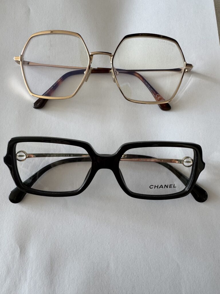 Två par glasögon på en vit yta: det övre paret har sexkantiga guldbågar och det undre paret har svarta rektangulära bågar med "CHANEL" skrivet på höger glas.