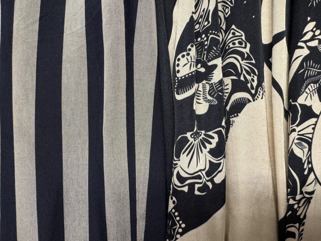 Närbild av två tyger: det ena med kraftiga vertikala ränder i svart och beige, det andra med ett intrikat blommönster i svart och beige. Texturerna och mönstren kontrasterar skarpt sida vid sida.