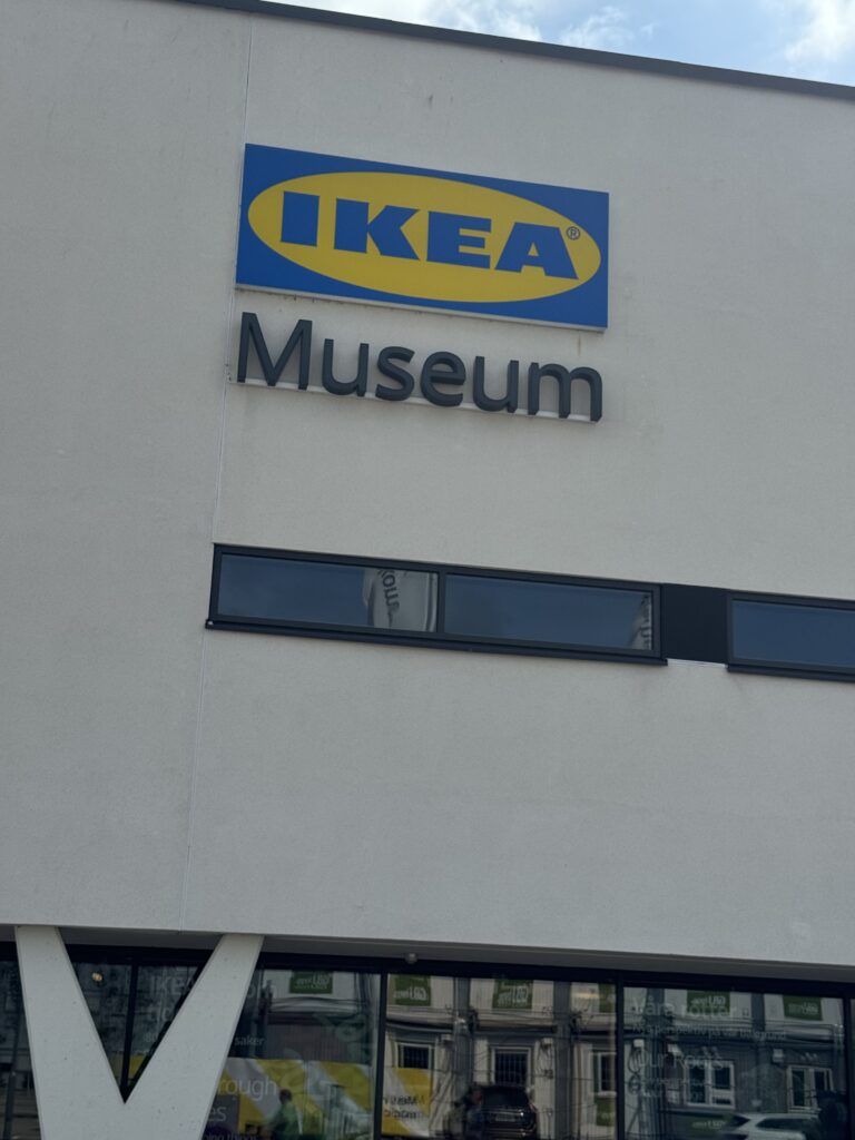 Utsidan av en vit byggnad med en blågul IKEA-logotypskylt ovanför ordet "Museum". Det finns två smala horisontella fönster under skylten och en partiell reflektion av byggnader syns i glaset.